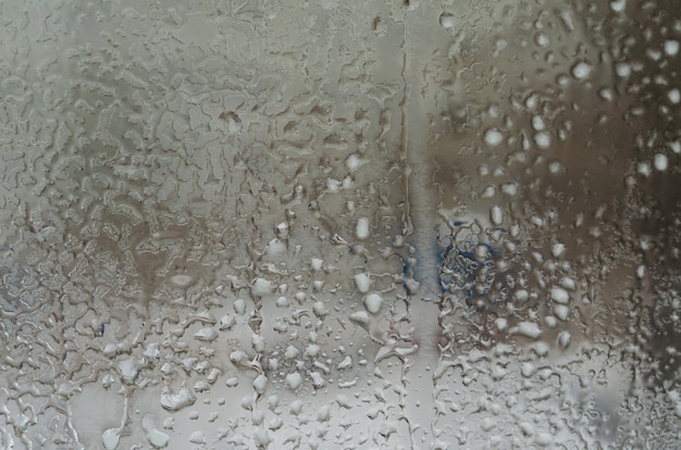 Gotas de lluvia y agua congelada en el fondo de cristal de la ventana