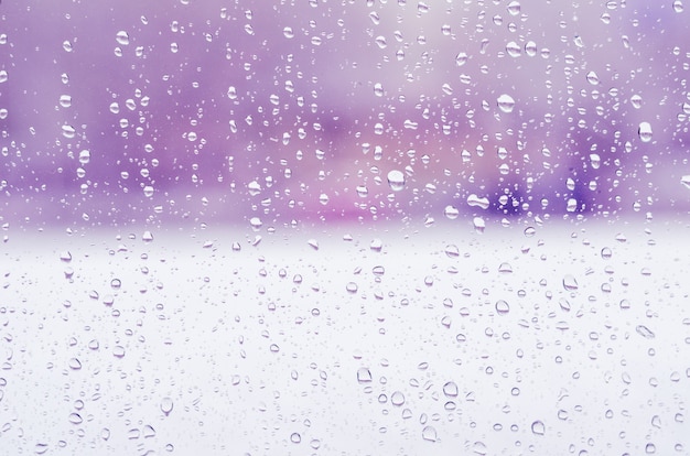 Gotas de lluvia y agua congelada sobre fondo de cristal de ventana, tono púrpura