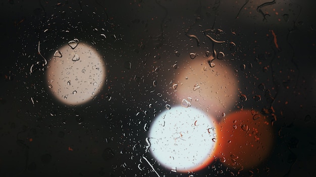 Gotas de lluvia caen por el cristal contra el fondo bokeh de coches en movimiento