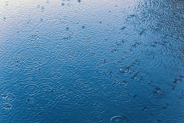 Gotas de lluvia en el fondo de la superficie del agua quieta con enfoque selectivo y desenfoque