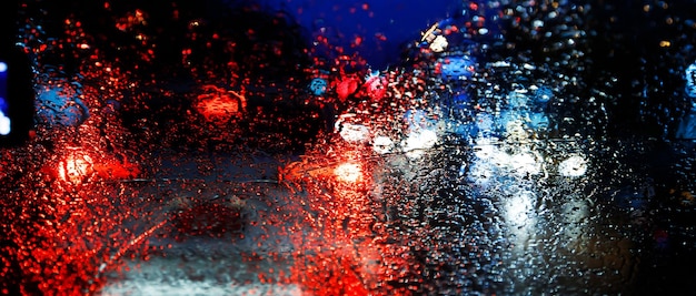 Gotas de lluvia llovizna en el parabrisas de vidrio en la noche. calle bajo la intensa lluvia. Luz trasera Bokeh. enfoque suave. Maneje con cuidado, camino resbaladizo. enfoque suave. coche de atasco.