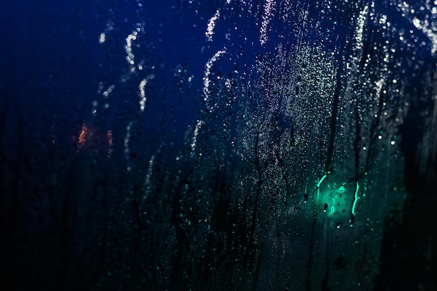 Gotas de lluvia y manchas en el vidrio por la noche en la ciudad