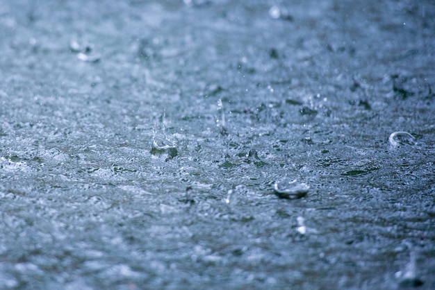 Gotas de lluvia ondeando en un charco con reflejo de cielo azul.