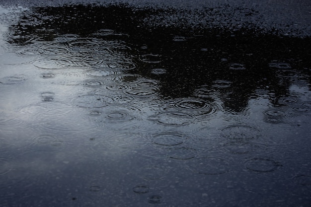 Gotas de lluvia y reflejo en un gran charco en la carretera asfaltada, fondo de la temporada de lluvias.