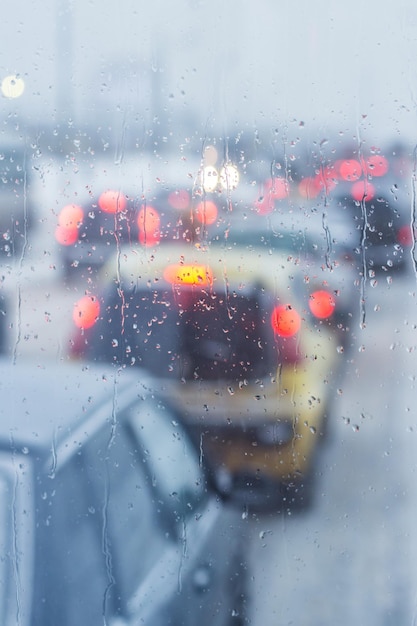 Gotas de lluvia sobre la ventanilla del coche. Atasco de tráfico borroso. Composición vertical