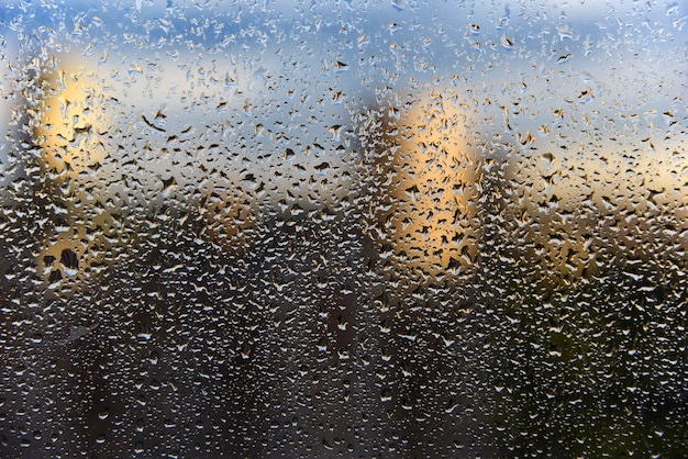 Gotas de lluvia sobre el vidrio de la ventana de cerca y el paisaje urbano fantasmal borroso.