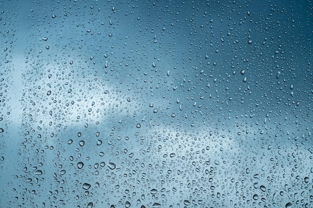 Foto gotas de lluvia en la superficie de los cristales de las ventanas con fondo de cielo azul borroso fondo natural de gotas de lluvia superposición abstracta para el diseño el concepto de mal tiempo lluvioso temporada de lluvias