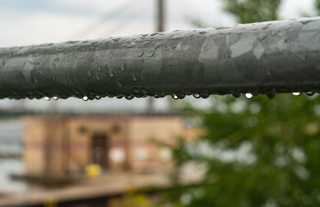 Gotas de lluvia en una tubería de metal gris después de la lluvia con una casa al fondo