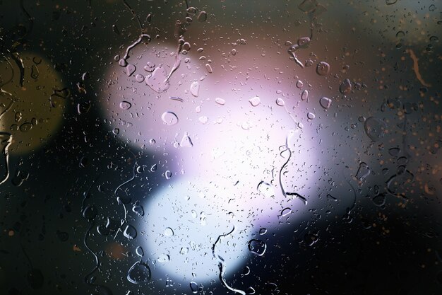 Gotas de lluvia en la ventana de un automóvil con fondo bellamente borroso de los semáforos de la calle