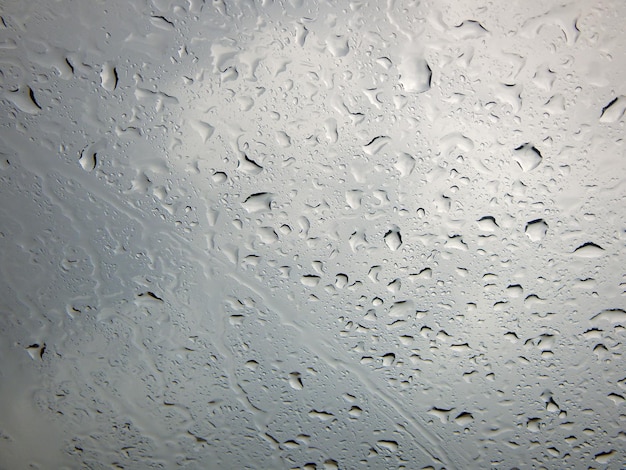 Foto gotas de lluvia en la ventana del coche en primer plano sobre un fondo gris