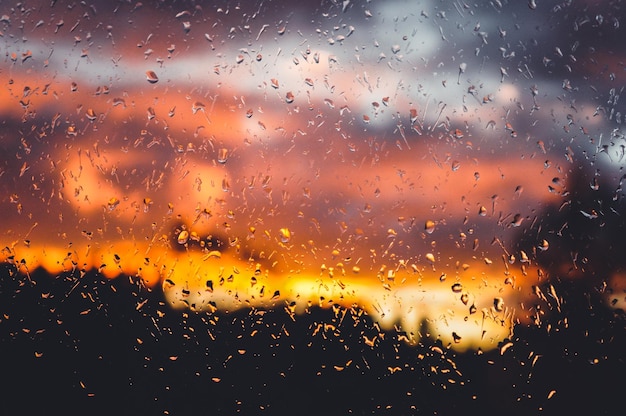 Gotas de lluvia en la ventana en el fondo de la puesta de sol naranja otoño y concepto de romance hermoso fondo
