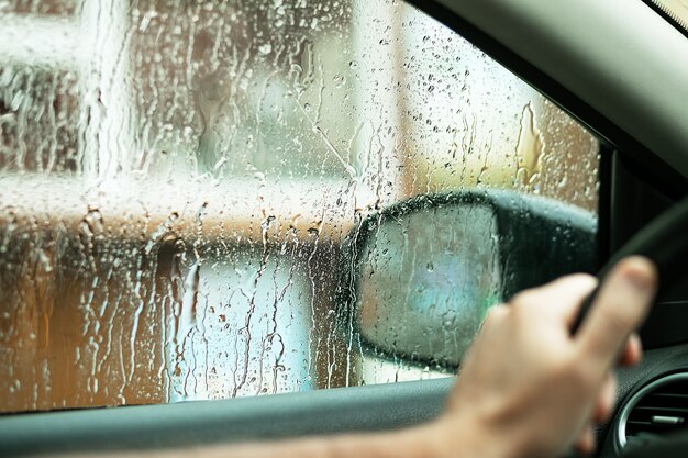 Gotas de lluvia en la ventana lateral del coche, el agua cae desde la ventana del conductor.