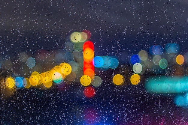 Gotas de lluvia en la ventana por la noche con luces bokeh. Fondo abstracto, gota de agua sobre el vidrio, luces de la ciudad por la noche.