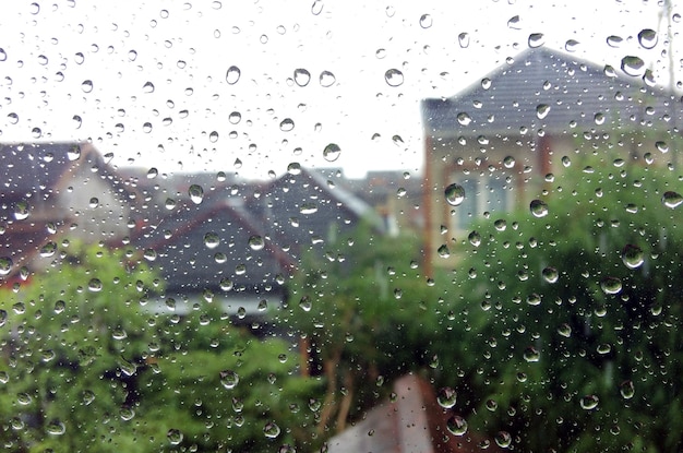 Gotas de lluvia en la ventana de vidrio con residentes borrosos y fondo de árboles