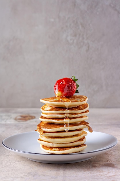 Las gotas de miel caen de las fresas a una pila de panqueques, sobre un fondo beige