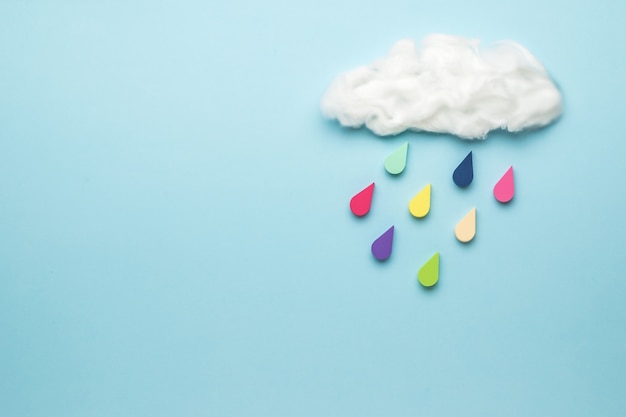 Gotas multicolores caen de una nube sobre una superficie azul