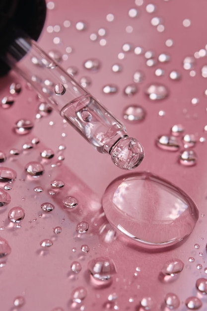 Gotas de pipeta y salpicaduras de agua micelar sobre un fondo rosado