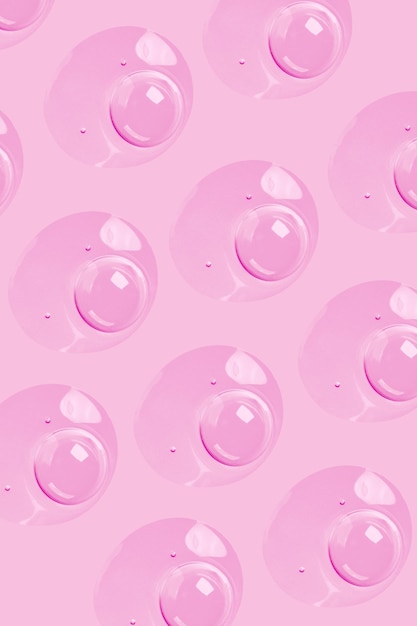 Gotas redondas de suero de gel transparente sobre un gel de fondo rosa con burbujas Gotas de agua