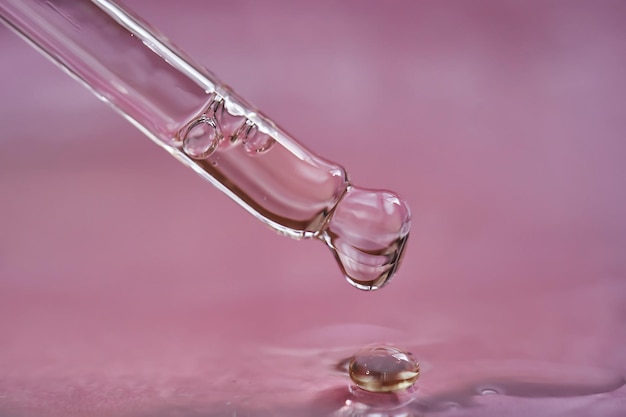 Gotas con suero o aceite cosmético sobre un fondo rosado