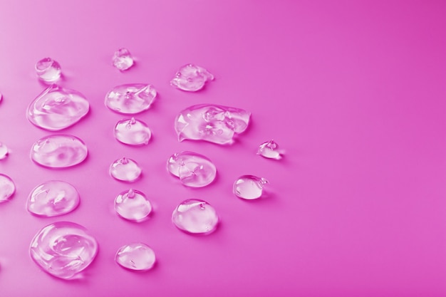 Gotas transparentes de gel em uma superfície rosa