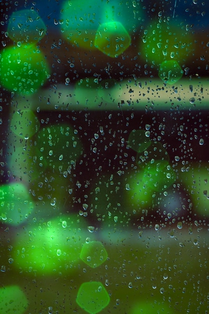 Gotas en la ventana y luces verdes de colores en la noche.