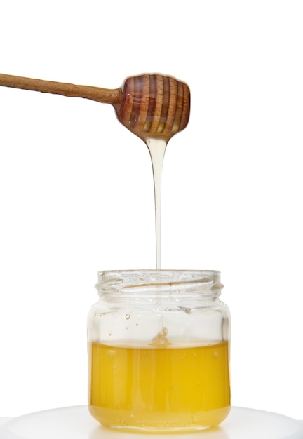 Goteo de miel del cucharón de miel en un tarro de miel natural dulce saludable orgánica, aislado sobre fondo blanco con espacio de copia