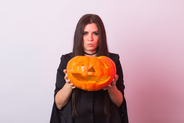 Gotische junge frau im hexenhalloween-kostüm mit einem geschnitzten kürbis.