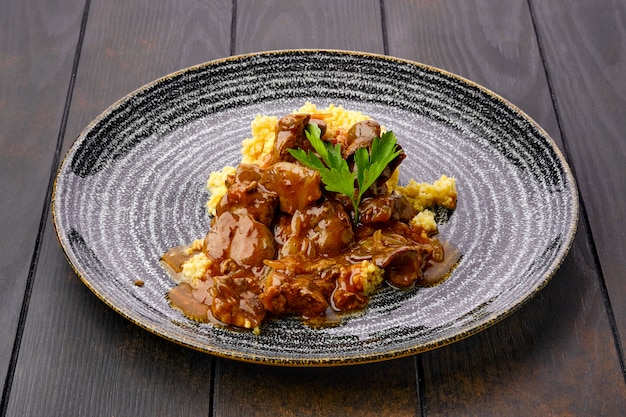 Goulash de carne com mingau de milho e molho cremoso na mesa de madeira escura