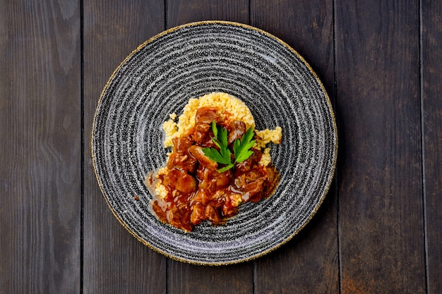 Goulash de carne com mingau de milho e molho cremoso na mesa de madeira escura