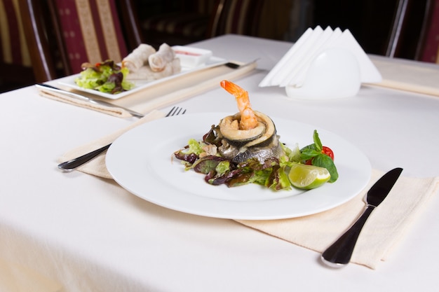 Gourmet-Meeresfrüchte-Gericht mit Fischfleisch und Garnelen auf Gemüse mit Zitrone. Vorbereitet auf weißer runder Platte. Auf dem Tisch im Restaurant serviert.