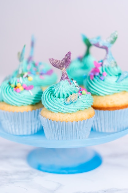 Gourmet-Meerjungfrauen-Cupcakes mit blauem Buttercreme-Zuckerguss und verziert mit Streuseln und Schokoladen-Meerjungfrauenschwänzen.