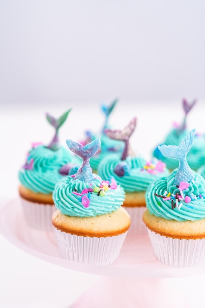 Gourmet-Meerjungfrauen-Cupcakes mit blauem Buttercreme-Zuckerguss und verziert mit Streuseln und Schokoladen-Meerjungfrauenschwänzen.