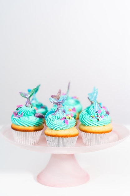 Gourmet-Meerjungfrauen-Cupcakes mit blauem Buttercreme-Zuckerguss und verziert mit Streuseln und Schokoladen-Meerjungfrauenschwänzen.