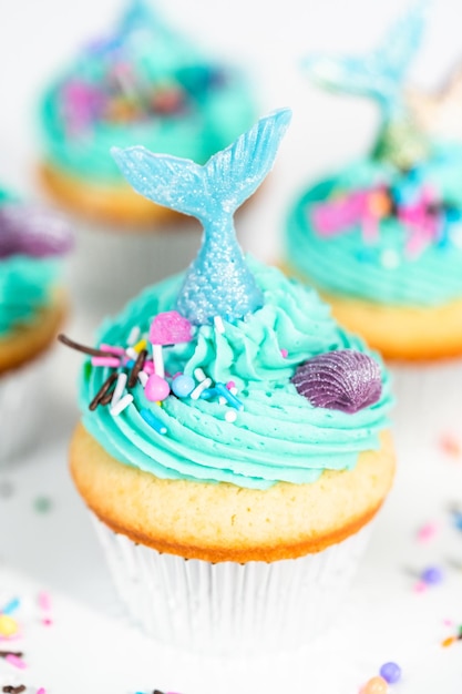 Gourmet-Meerjungfrauen-Cupcakes mit blauem Buttercreme-Zuckerguss und verziert mit Streuseln und Schokoladen-Meerjungfrauenschwänzen.
