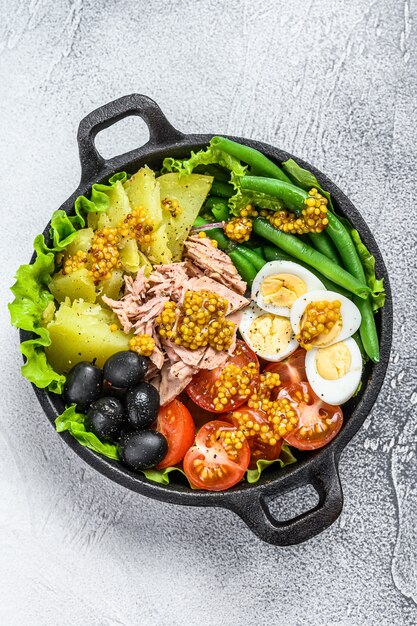 Gourmet-Nicoise-Salat mit Gemüse, Eiern, Thunfisch und Sardellen in einer Pfanne. Weißer Hintergrund. Ansicht von oben.