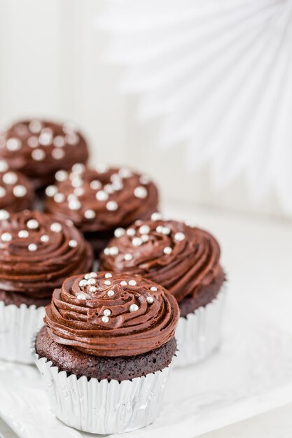 Gourmet-Schokoladen-Cupcakes verziert mit silbernen Kugeln auf Schokoladenglasur.