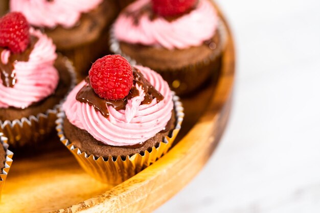 Gourmet-Schokoladen-Himbeer-Cupcakes, beträufelt mit Schokoladenganache und garniert mit einer frischen Himbeere.