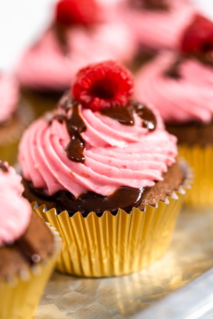 Gourmet-Schokoladen-Himbeer-Cupcakes, beträufelt mit Schokoladenganache und garniert mit einer frischen Himbeere