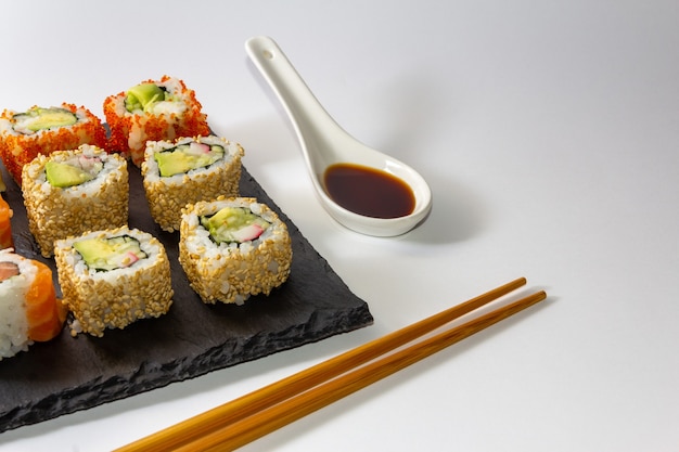 Gourmet-Sushi-Tablett auf Schieferoberfläche auf weißem Hintergrund mit Sojasauce und Stäbchen Textfreiraum