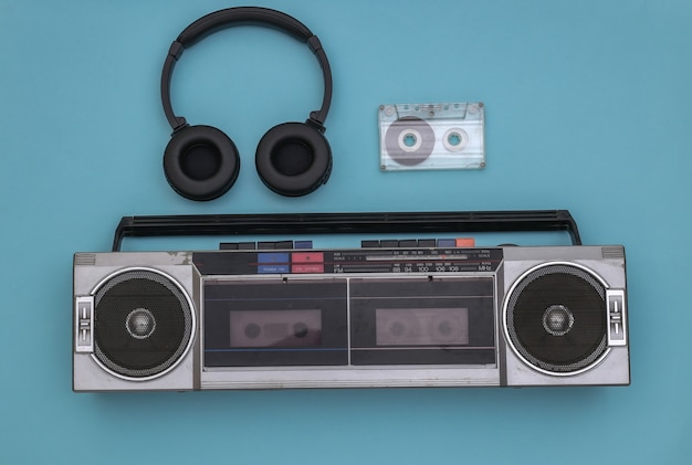 Grabadora de cinta de audio Boombox, auriculares estéreo y casete de audio sobre un fondo azul. Retro de los 80. Vista superior. Endecha plana