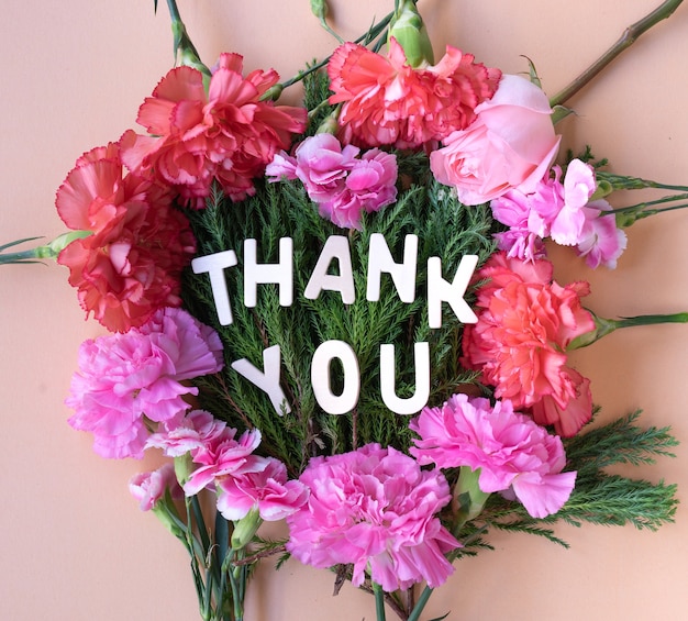 Gracias palabra de madera en el marco de claveles de flores frescas sobre fondo rosa crema suave