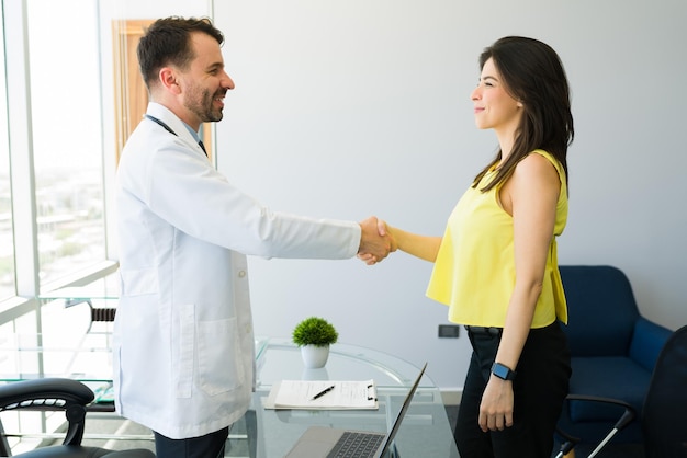 Foto gracias por su amable trato. apuesto doctor saludando a un caucásico. paciente femenino que llega a la oficina del especialista médico para un diagnóstico