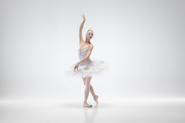 Graciosa bailarina clássica dançando isolada no fundo branco do estúdio. mulher com roupas macias, como personagens de um cisne branco. o conceito de graça, artista, movimento, ação e movimento. parece leve.