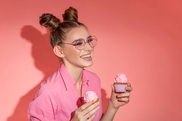 Graciosa mujer sonriente con camisa rosa sosteniendo panecillos con fondo rosa. Dulces dulces humor. Luz dura. Copie el espacio.