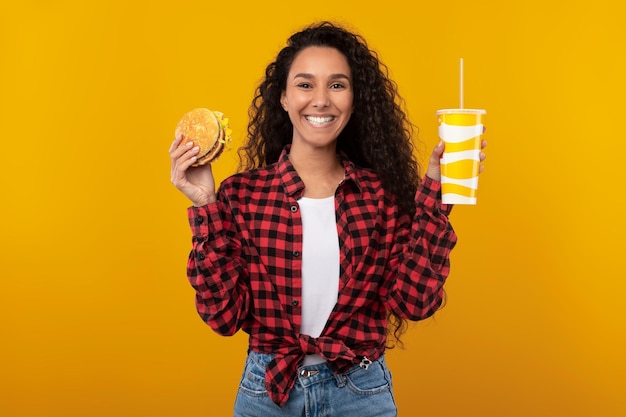 Graciosa señorita sosteniendo hamburguesa y bebida