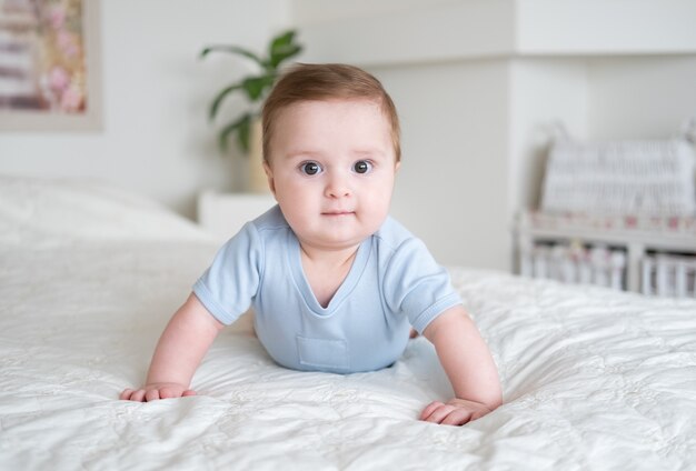 Gracioso bebé de 6 meses de edad en traje azul sonriendo y acostado en la cama en casa