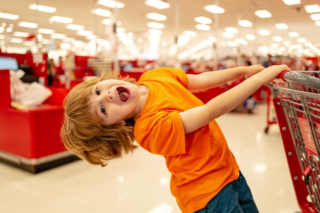 Gracioso cliente niño niño holdind carrito de compras en el supermercado tienda de abarrotes lindo niño niño con s