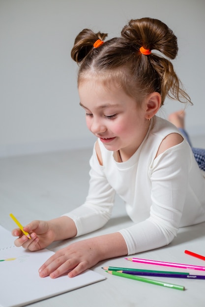 Gracioso dibujo de niña en un álbum con lápices de colores educación en el hogar jardín de infantes