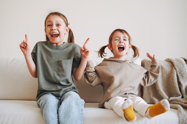 Gracioso feliz dos niños niñas hermanas divirtiéndose en el sofá en el hogar