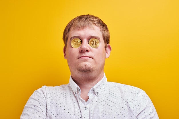 Foto gracioso gordo con bitcoins en los ojos sobre el fondo amarillo. concepto de dinero digital virtual, codicia, vanidad, riqueza y tacañería